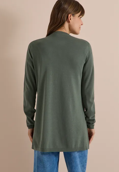 Vrouw van achteren in een groene lange cardigan en blauwe jeans.