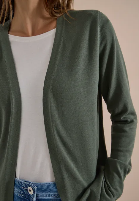 Iemand draagt een open olijfgroene cardigan over een wit T-shirt.