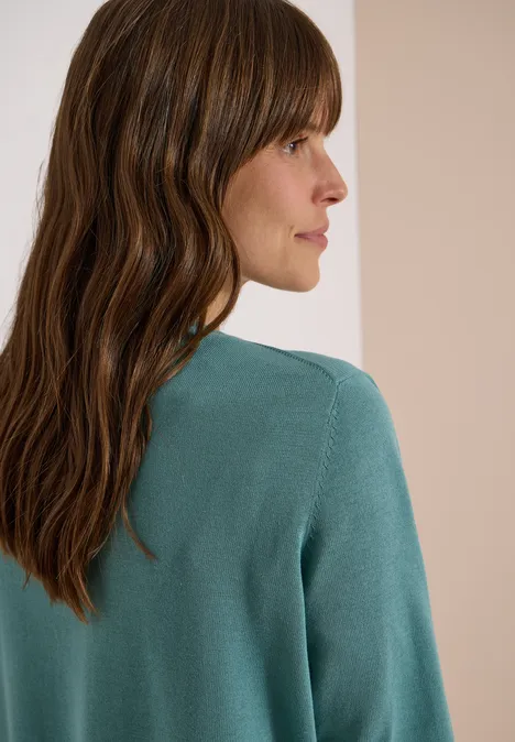 Zijaanzicht van een vrouw met lang bruin haar en een turquoise trui.
