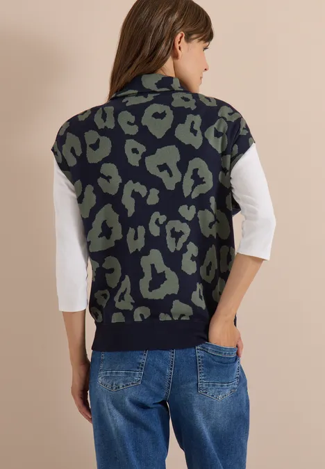 Frau von hinten in weißem Shirt, grün-schwarzer Animal-Print-Weste und lockerer Jeans.