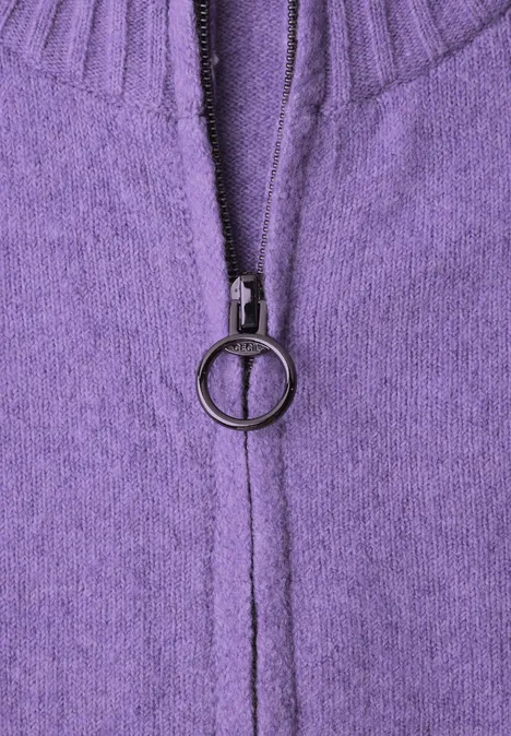 Nahaufnahme eines lila Strickpullovers mit Reißverschluss und rundem Zipperanhänger.