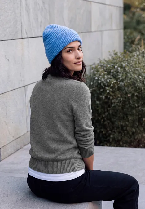 Langarm Cardigan mit Rundhals und Zipper flint grey melange Eine junge Frau mit blauer Strickmütze und grauem Pullover sitzt an einer Steinwand und blickt über die Schulter.