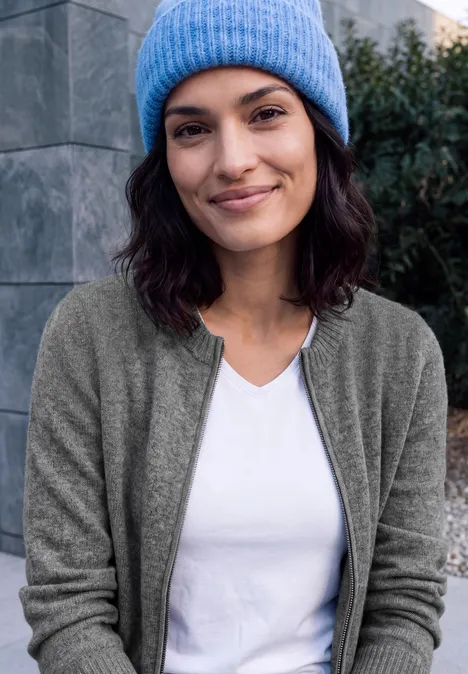 Langarm Cardigan mit Rundhals und Zipper flint grey melange Eine lächelnde Frau trägt eine blaue Mütze, weiße Shirt und graue Strickjacke im Outdoor-Umfeld.