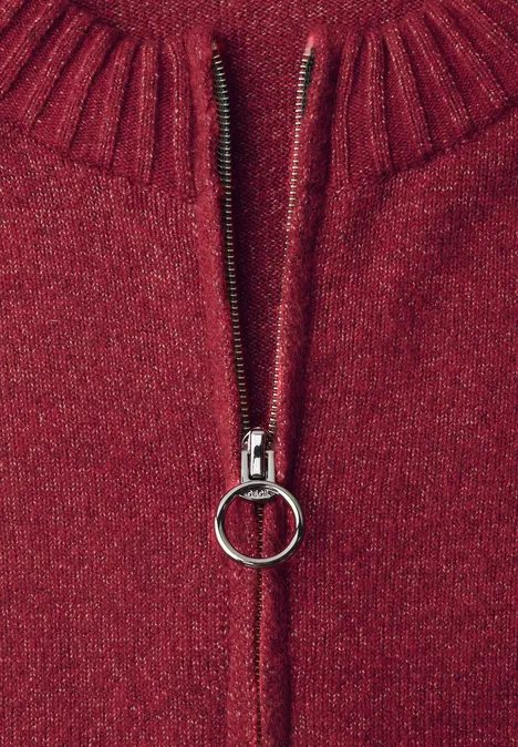 Nahaufnahme eines roten Strickpullovers mit silbernem Reißverschluss und rundem Zipper-Anhänger.