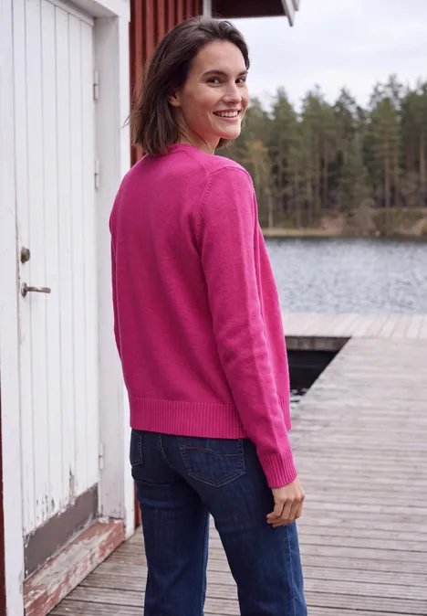 Langarm Cardigan mit Rundhals und Zipper pink flash Frau in pinkem Pullover blickt lächelnd über die Schulter auf einem Steg am See vor Waldkulisse.