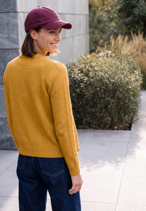 Cardigan zippé à manches longues et col rond golden honey melange Eine Frau in gelbem Pullover und roter Kappe steht auf einer Terrasse und blickt über die Schulter.