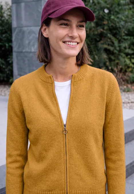 Cardigan zippé à manches longues et col rond golden honey melange Eine junge Frau mit roter Cap und senfgelbem Pullover lächelt im Freien.