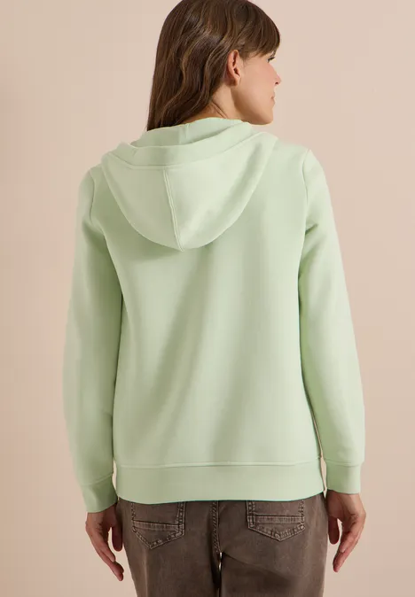 Person von hinten in hellgrüner Kapuzenjacke und Jeans.
