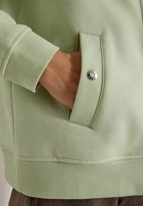 Hand steckt in der Vordertasche eines hellgrünen Hoodies mit Druckknopf