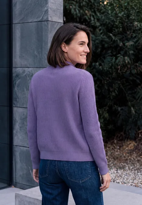 Cardigan mit Stehkragen und Zipper pastel lilac melange Eine Frau in einem lilafarbenen Pullover und Jeans steht im Freien und blickt lächelnd seitlich über die Schulter.