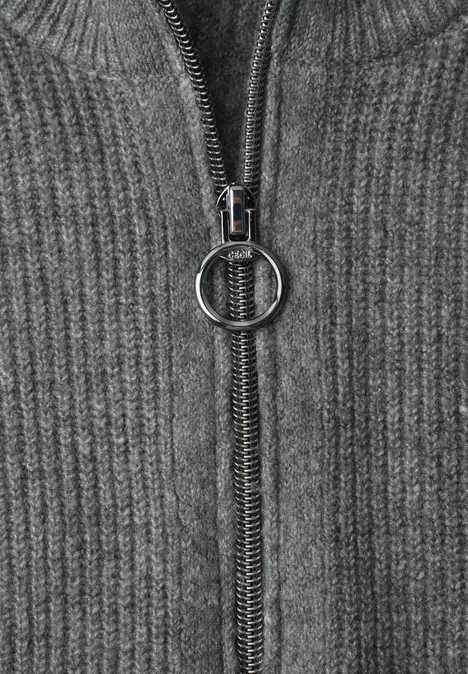 Nahaufnahme eines grauen Strickpullovers mit Reißverschluss und rundem Zipper-Anhänger.