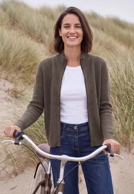 Cardigan mit Stehkragen und Zipper mushroom taupe melange Lächelnde Frau mit Fahrrad vor Dünen, trägt Jeans, weißes Shirt und grüne Strickjacke.