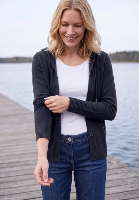 Langarm Cardigan mit Kapuze urban dark blue Frau steht lächelnd auf einem Holzsteg am See, trägt Jeans, weißes Shirt und schwarze Strickjacke.