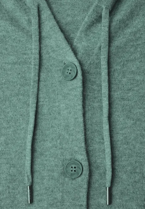 Close-up van een groene gebreide cardigan met knopen en capuchonkoorden.