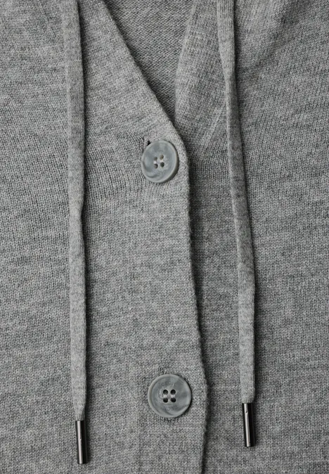 Close-up van een grijze gebreide cardigan met capuchon, knopen en koordjes.