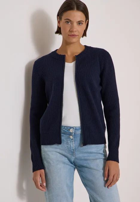 Femme en cardigan bleu marine, top blanc et jean sur fond clair.