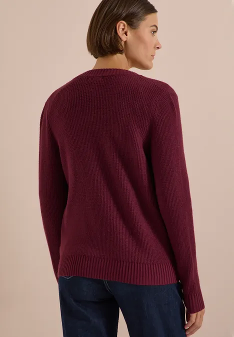 Une femme vue de dos porte un pull bordeaux et un jean bleu.