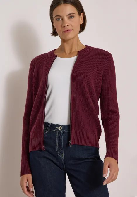 Une femme porte un cardigan bordeaux, un t-shirt blanc et un jean bleu.