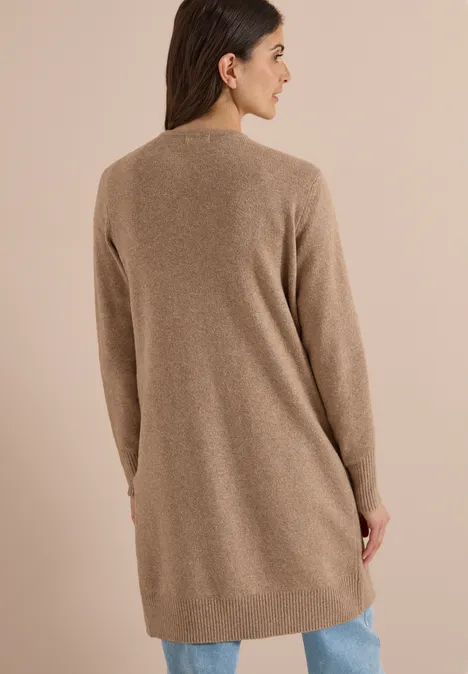 Achteraanzicht van een vrouw in een lange, beige gebreide cardigan en spijkerbroek.