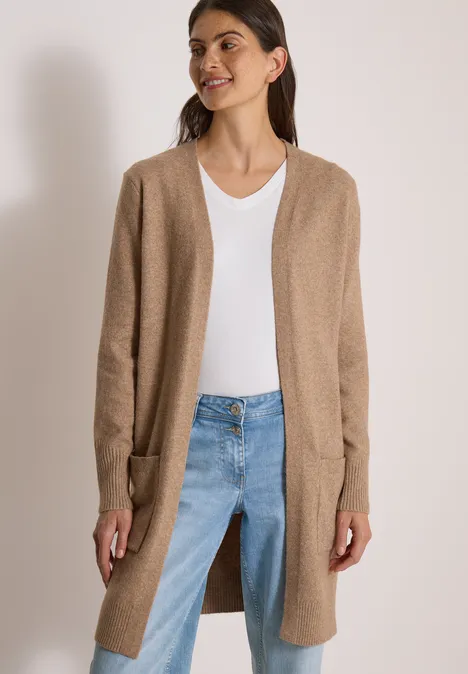 Vrouw in een lange beige cardigan, wit t-shirt en blauwe jeans, casual look.