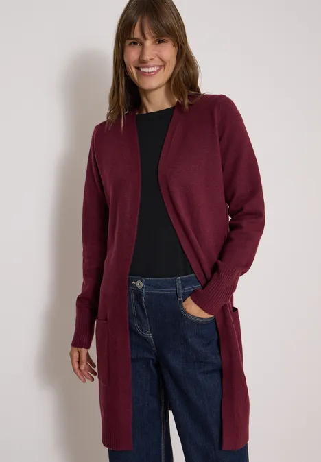 Cardigan long à la coupe ample red wine Femme souriante portant un cardigan bordeaux, un t-shirt noir et un jean devant un fond blanc
