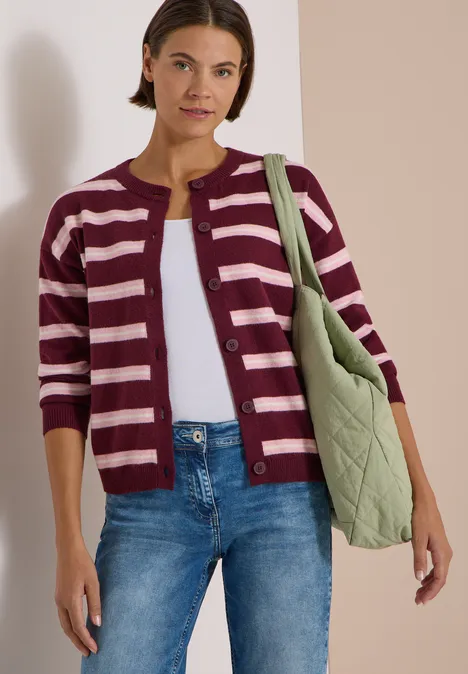 Femme en cardigan rayé, jean et sac matelassé vert.