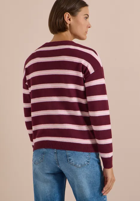 Femme portant un pull à rayures bordeaux et blanc et un jean, vue de dos sur fond clair.