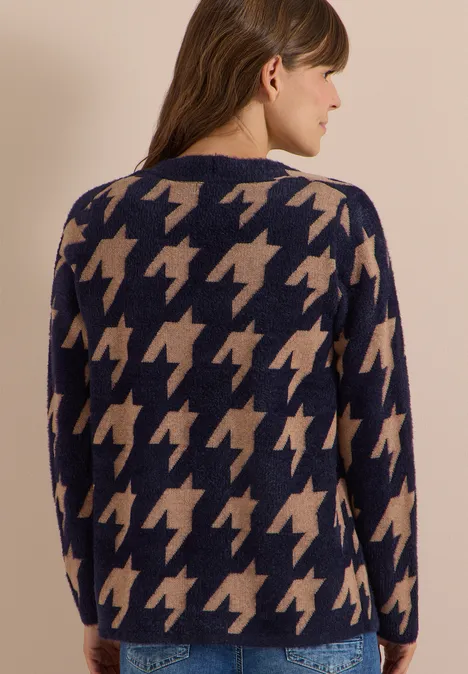 Femme de dos portant un pull bleu marine à motif pied-de-poule beige sur fond clair.