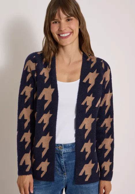 Femme souriante portant un cardigan pied-de-poule bleu marine et beige, top blanc et jean.