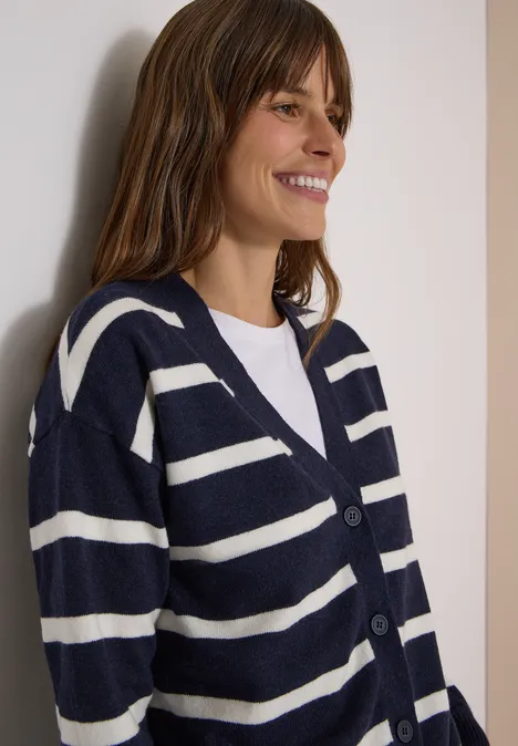 Vest met V-hals en strepen urban dark blue melange Frau lächelt und trägt einen marineblauen Cardigan mit weißen Streifen und ein weißes Shirt.