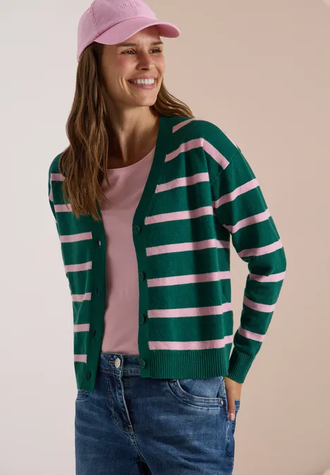 Vest met V-hals en strepen dark fir green melange Eine lächelnde Frau im grünen, weiß gestreiften Cardigan, rosa Shirt und Jeans trägt eine rosa Cap.