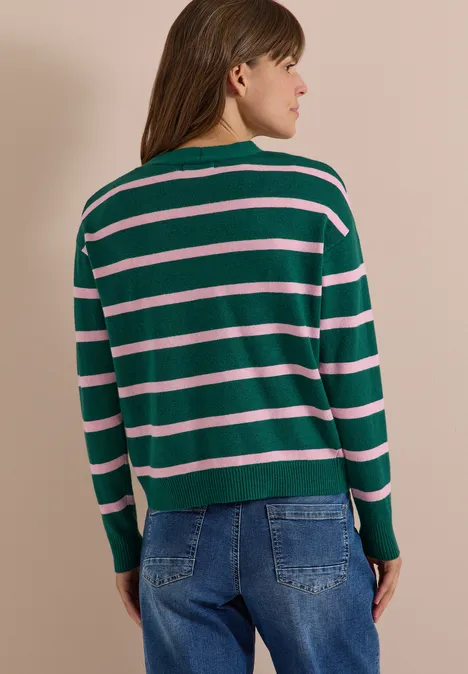 Vest met V-hals en strepen dark fir green melange Frau steht von hinten in grün-rosa-gestreiftem Pullover und Jeans vor neutralem Hintergrund.