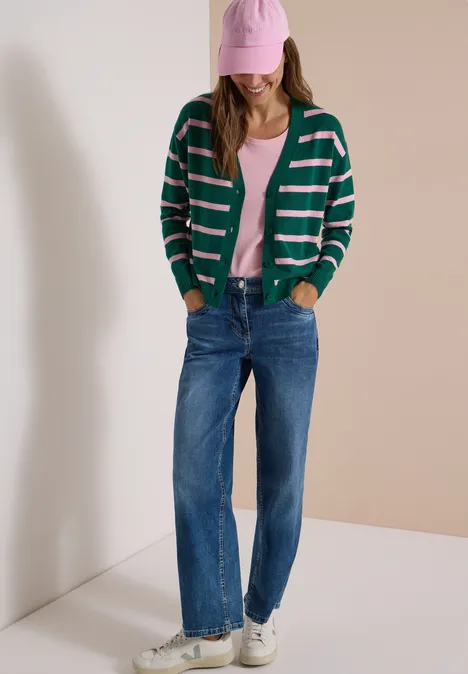 Vest met V-hals en strepen dark fir green melange Frau in grün-weiß gestreifter Strickjacke, rosa Top, blauen Jeans, weißen Sneakers und rosa Cap.
