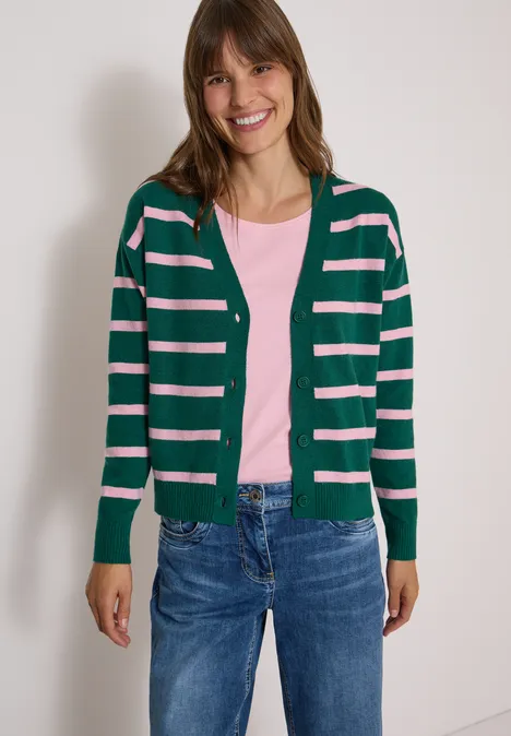 Vest met V-hals en strepen dark fir green melange Junge Frau steht vor weißer Wand, lächelt, trägt Jeans, rosa Shirt und dunkelgrün-rosa gestreifte Strickjacke.