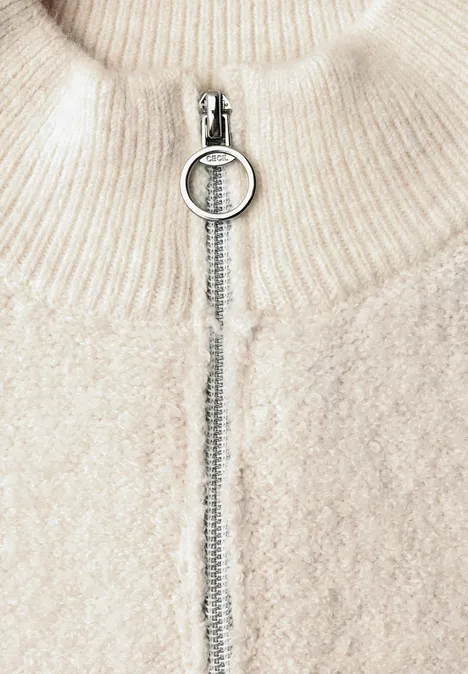 Cremefarbener Grobstrickpullover mit Stehkragen und silbernem Ringzipper.