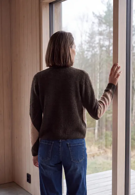 Cardigan mit V-Neck und Argyle-Muster truffle brown Eine Frau steht im Holzhaus am Fenster und blickt auf den Wald.