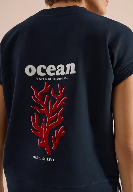 Dunkelblaues Shirt mit Aufdruck 'ocean' und rotem Korallenmotiv am Rücken.