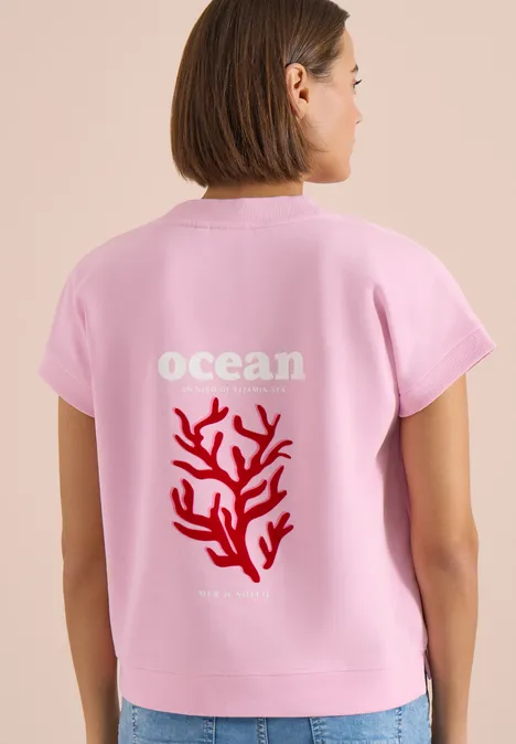 Frau von hinten mit pinkem T-Shirt, Schriftzug 'ocean' und rotem Korallenmotiv