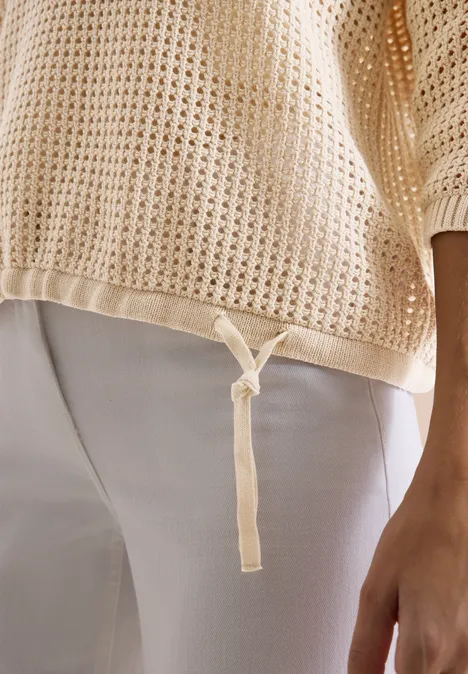 Beige locker gestricktes Top mit Kordel am Saum zu weißen Hosen kombiniert.