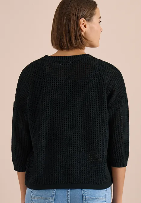 Rückenansicht einer Person in schwarzem grob gestricktem Pullover mit 3/4-Ärmeln vor beigem Hintergrund