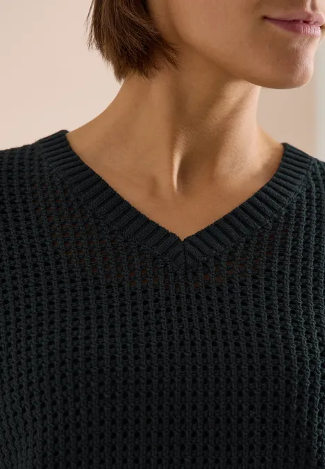 Nahaufnahme eines Oberkörpers in grobem schwarzen Strickpullover mit V-Ausschnitt.