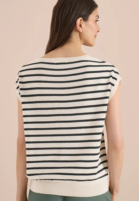 Frau von hinten in weiß-blau gestreiftem kurzärmligem Shirt vor beigem Hintergrund.