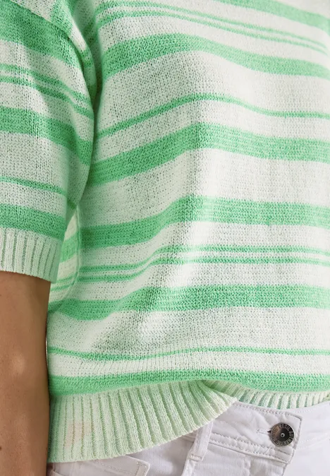 Nahaufnahme eines grün-weißen gestreiften Pullovers über einer weißen Hose.