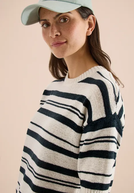 Frau mit Baseball-Cap und gestreiftem Schwarz-Weiß-Pullover, sichtbarer Ohrring