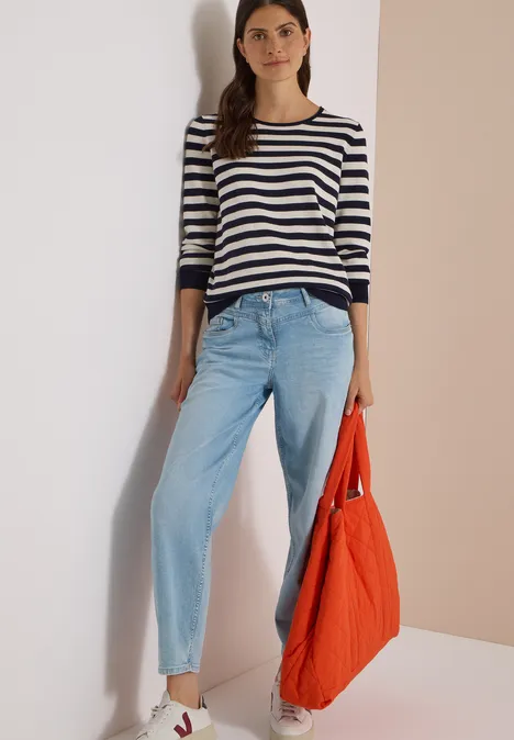 Pull à col rond et rayé urban dark blue Frau in gestreiftem Oberteil und hellblauen Jeans, hält eine große orange Tasche.
