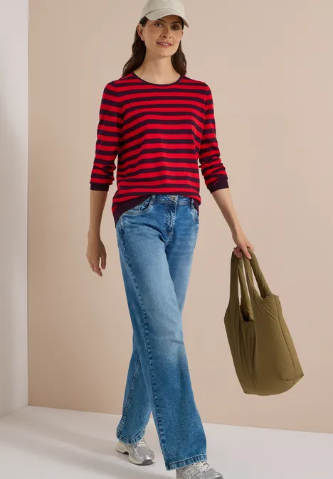Pull à col rond et rayé eggplant red Frau trägt rote-schwarz gestreifte Bluse, weite Jeans, Cap und grüne Tasche.
