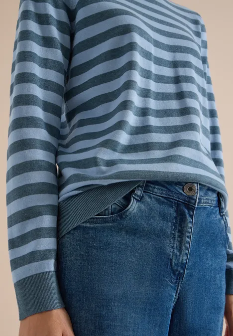 Gros plan d'une personne portant un pull rayé bleu et gris et un jean.