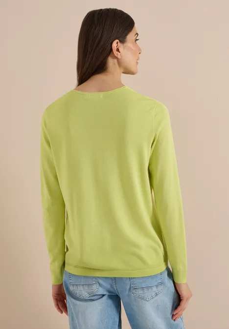 Rückansicht einer Person mit hellem Grünpullover und blauen Jeans vor beigem Hintergrund.
