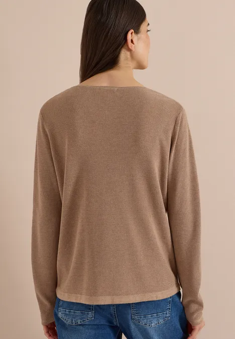Frau von hinten in beige Pullover und blauen Jeans, steht vor hellem Hintergrund.