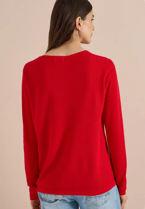 Frau von hinten in rotem Pullover und Jeans vor neutralem Hintergrund